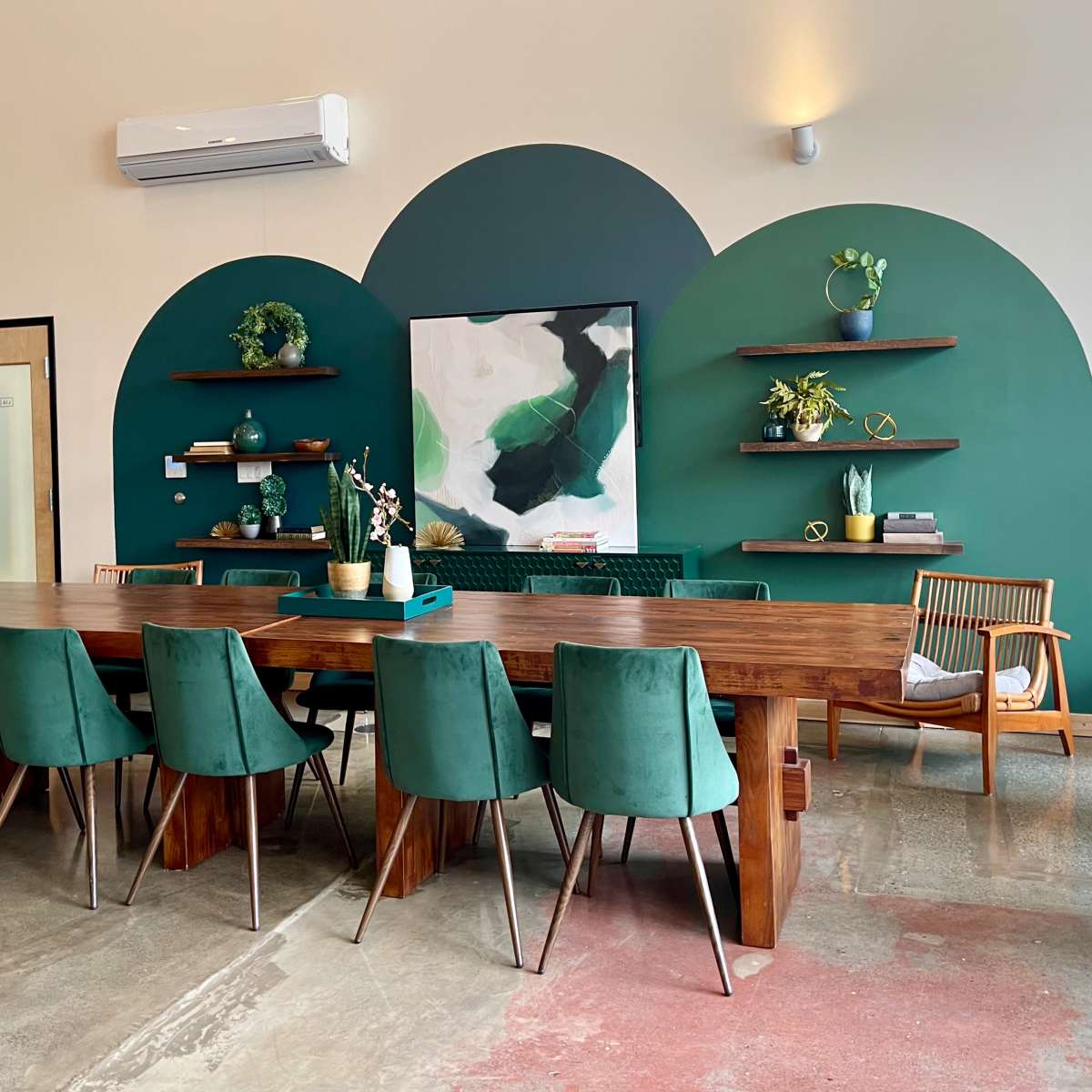 A wooden dining table with green chairs is set against a wall featuring two large green arches and shelves displaying decorative items.