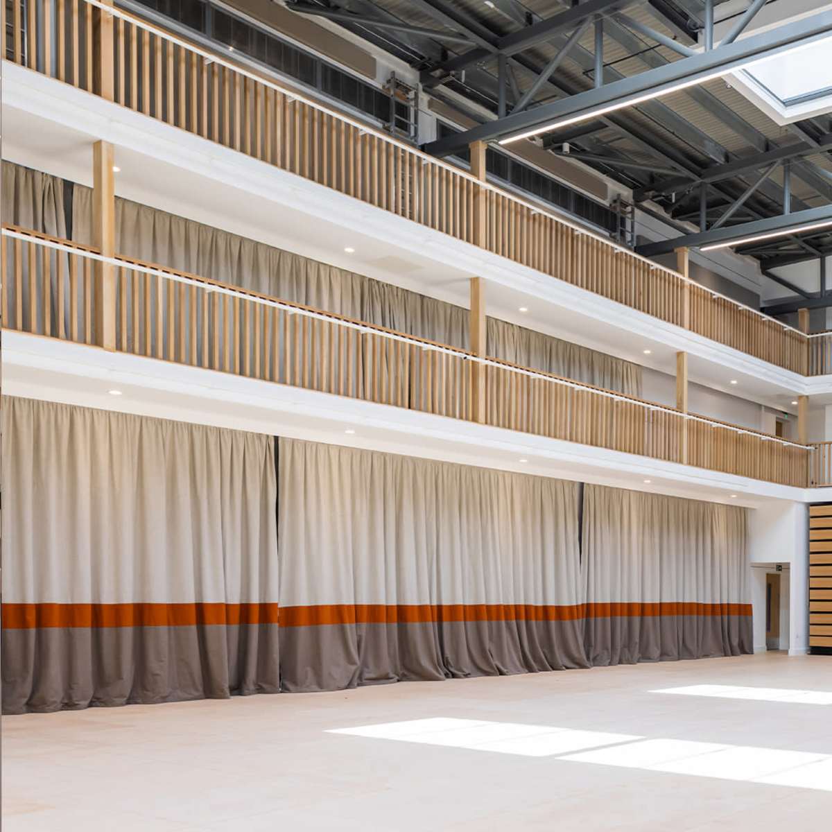 A spacious indoor venue with multiple levels, featuring wooden railings, large curtains, and a wall lined with wooden panels.