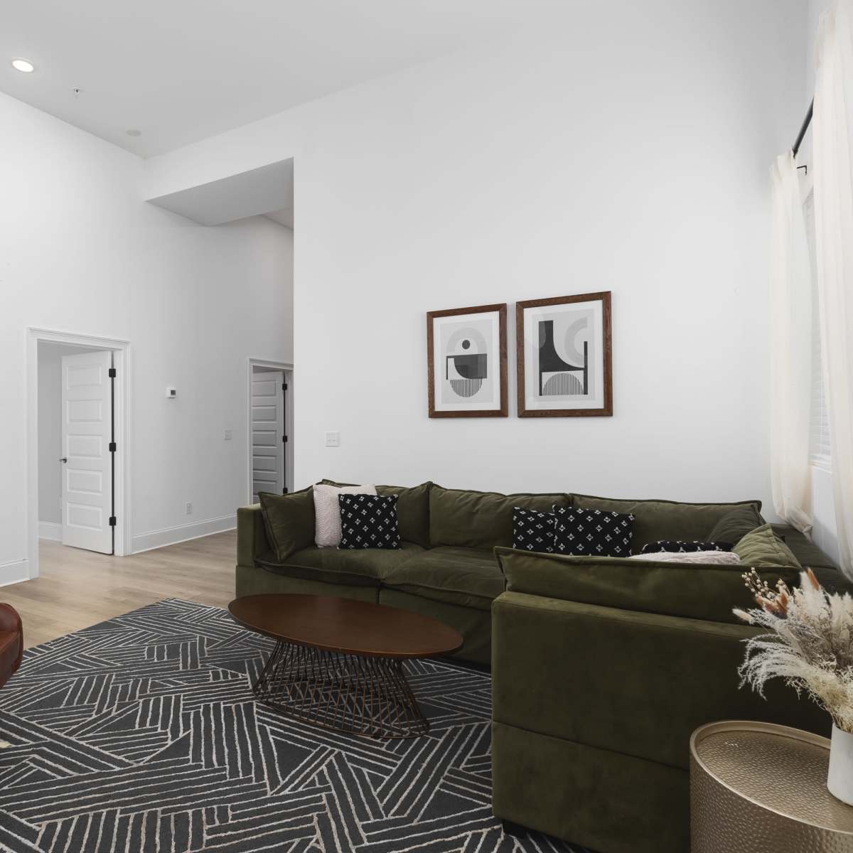 A modern living room features a green sofa, a brown accent chair, a round coffee table, and framed artwork on the walls.