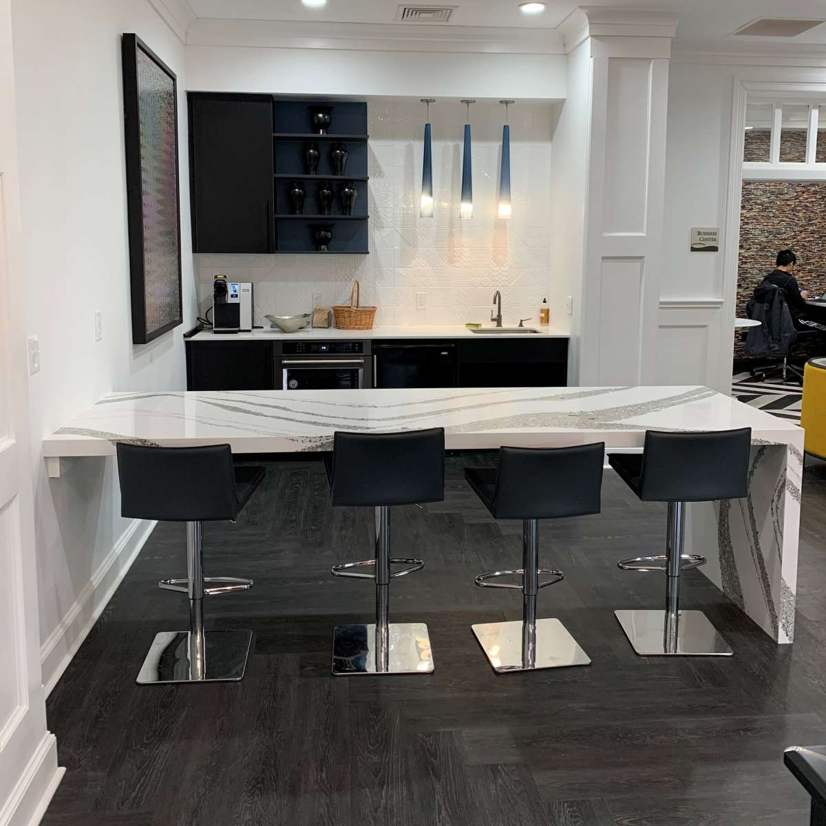 A modern kitchen area featuring a curved countertop with four black bar stools and a streamlined design.