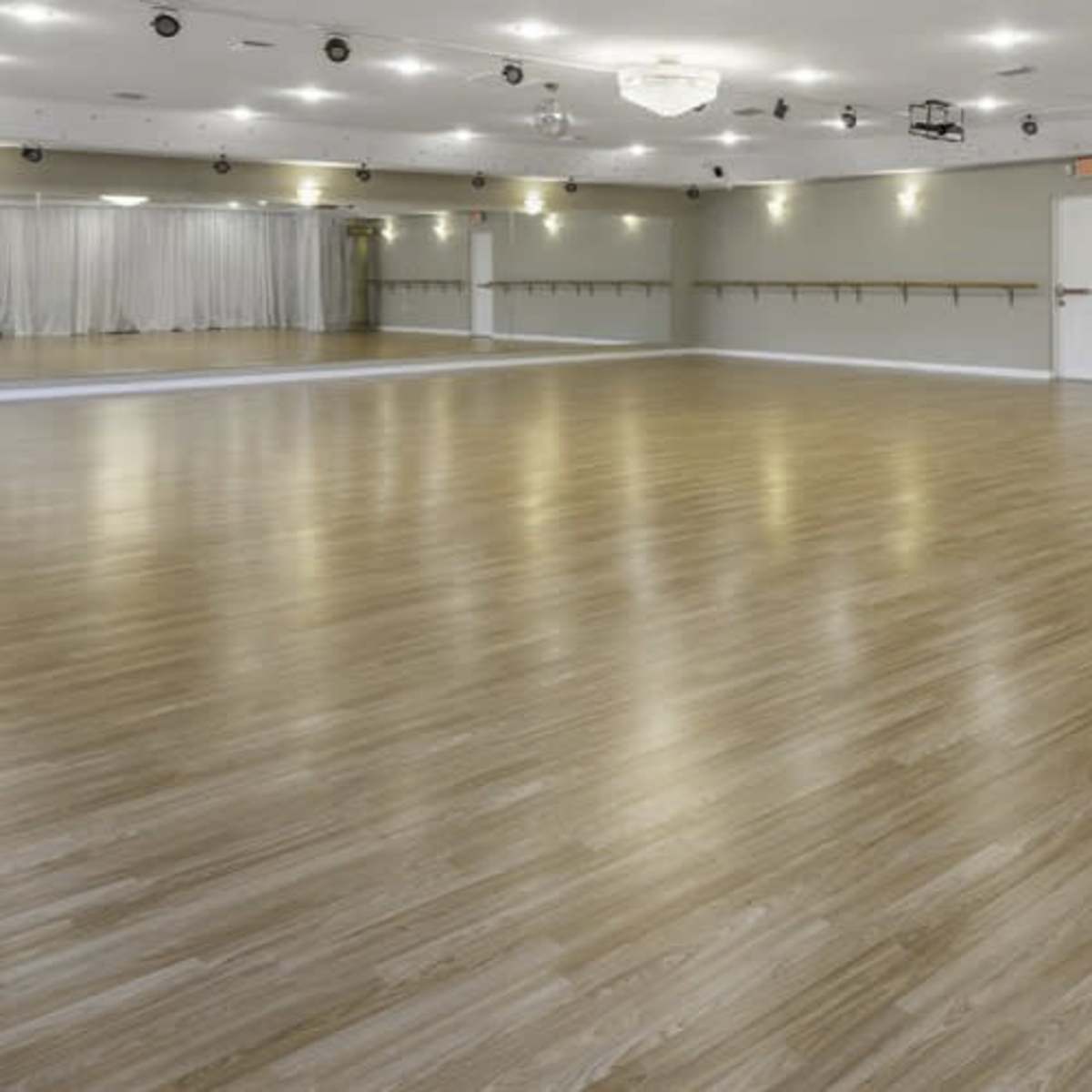 A spacious dance studio with a polished wooden floor and mirrored wall fixtures.