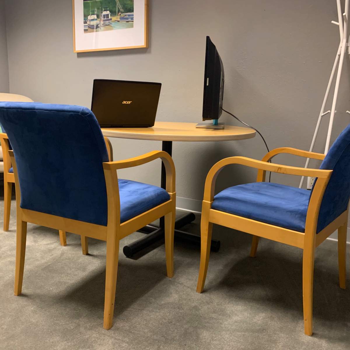 A small seating area with two blue chairs and a round table, accompanied by a laptop and a monitor on the table.