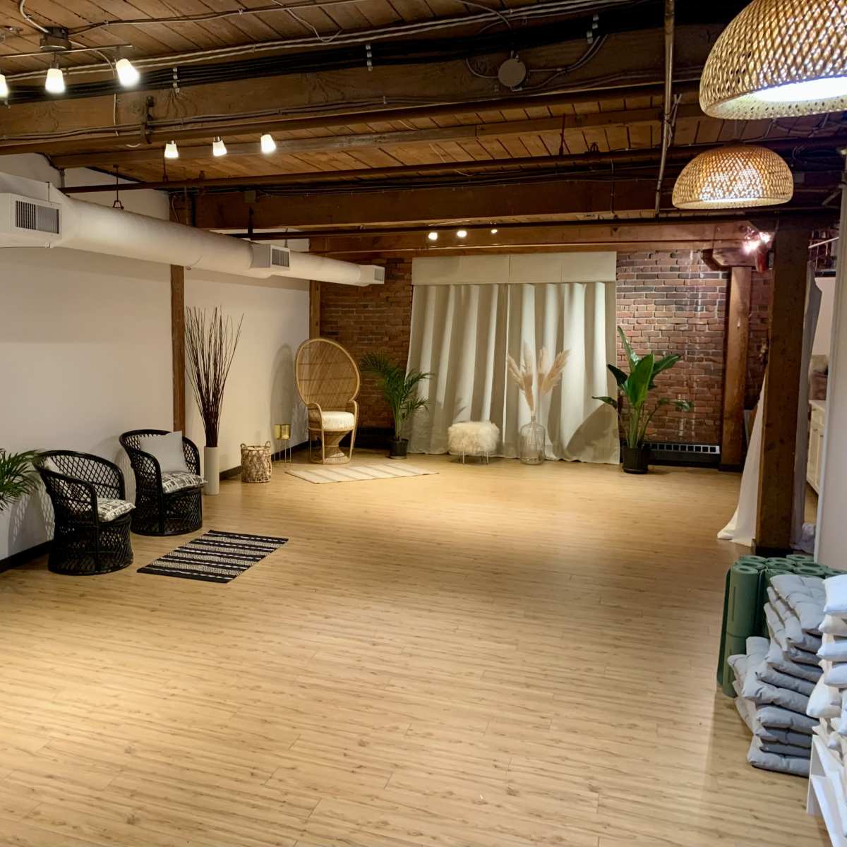 A spacious, well-lit room with wooden beams, featuring minimalist decor, plants, seating areas, and a soft color palette.