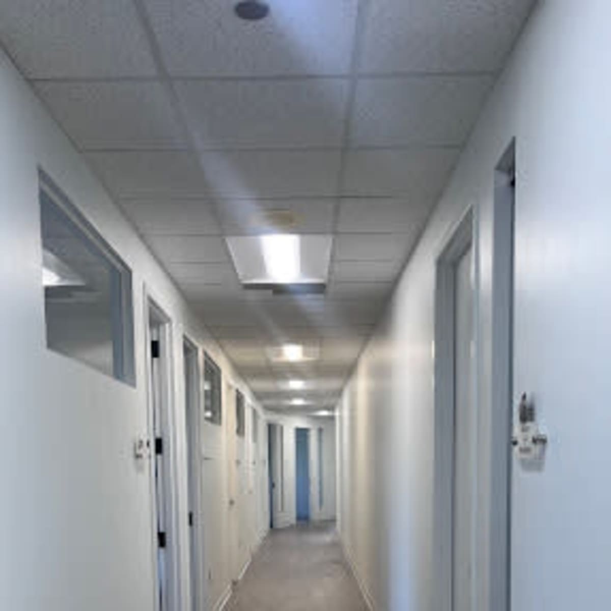 A long, narrow hallway lined with white doors and illuminated by overhead lights.