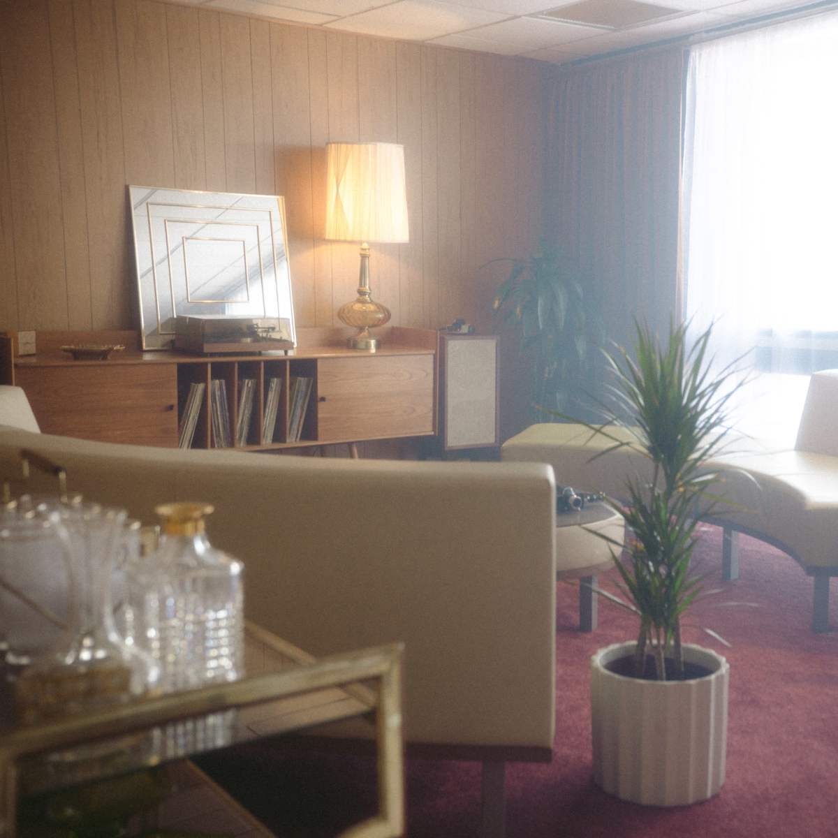 A vintage-style living room with two curved sofas, a tall lamp, a potted plant, and a wooden cabinet, all under soft lighting.