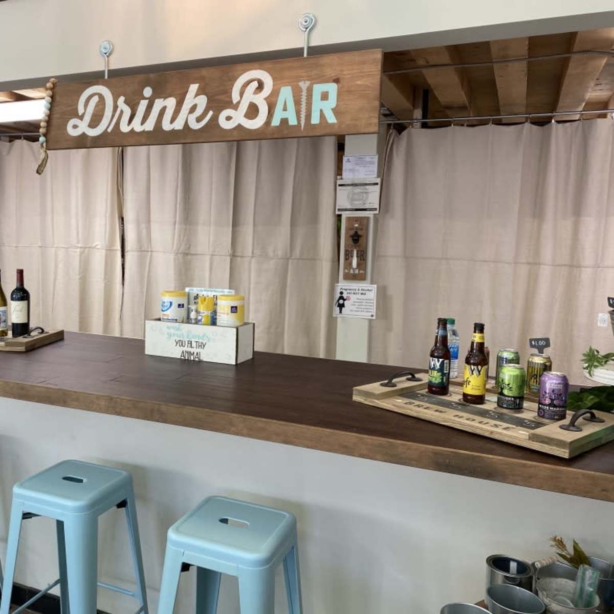 A drink bar with various bottles of wine and craft beverages displayed on wooden trays, under a sign that reads "Drink Bar."