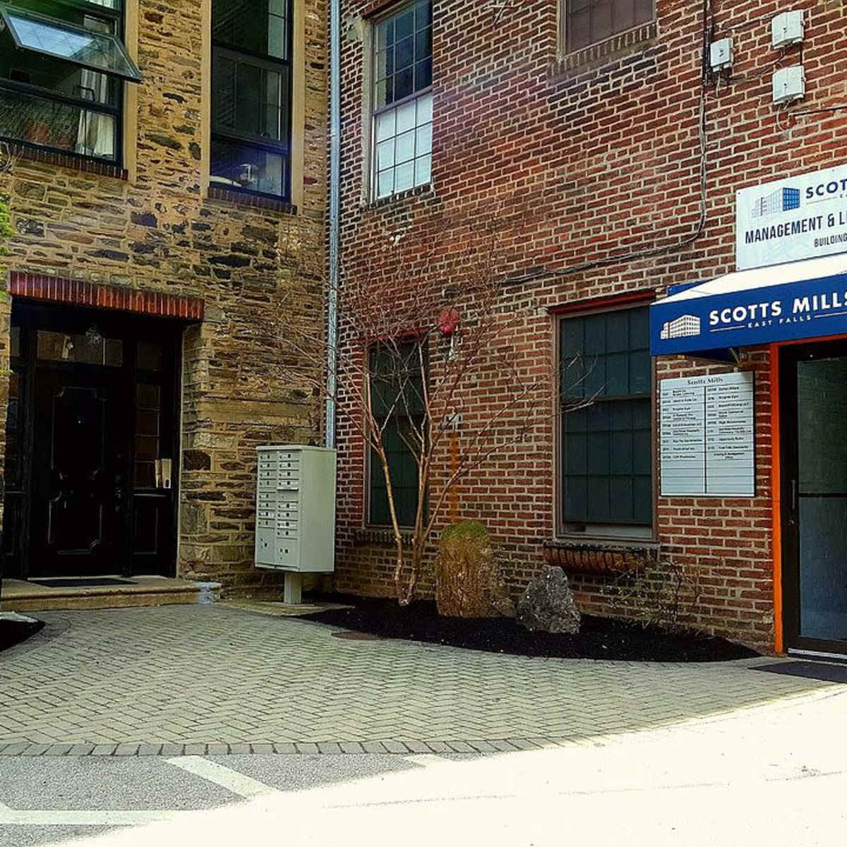 A brick building entrance with a mailbox on the side and a sign for Scott's Mill Management.