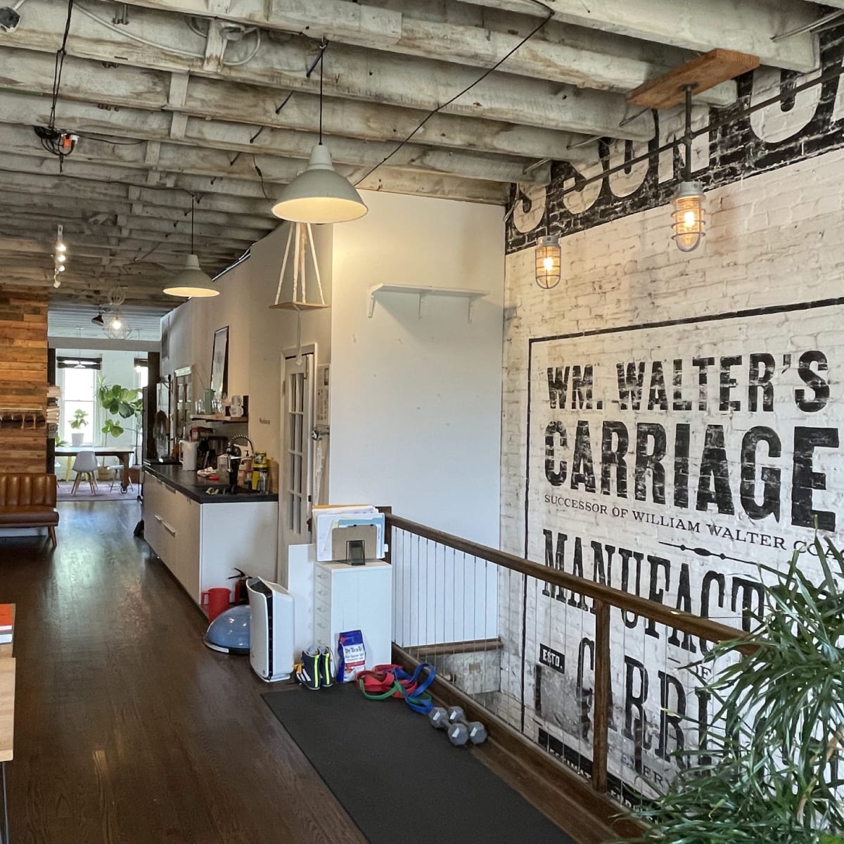 An open office space with wooden beams, a mix of modern and rustic decor, desks with computers, and exercise equipment in the corner.
