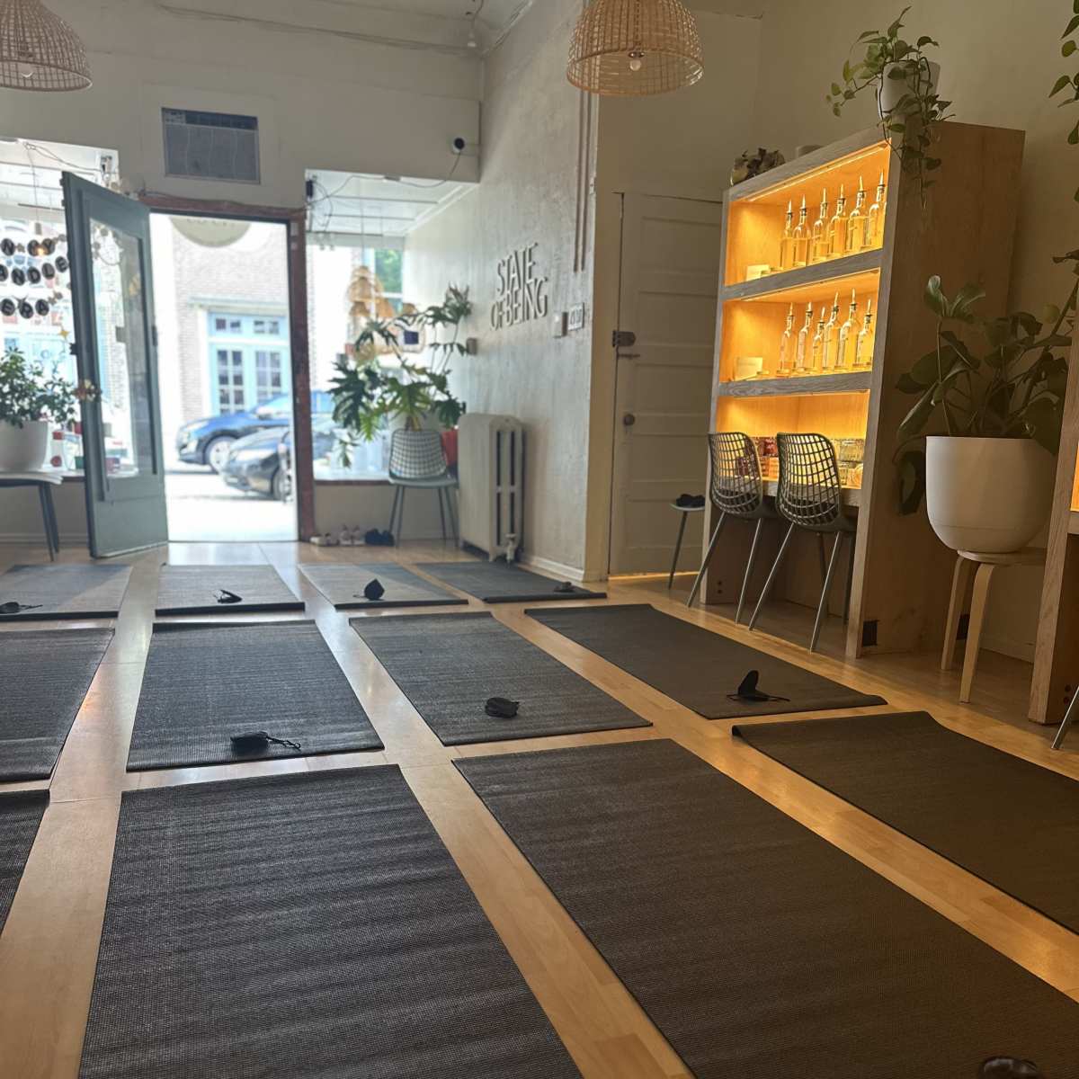 A yoga studio with several mats arranged on a wooden floor, and a reception area featuring plants and a backlit display shelf.