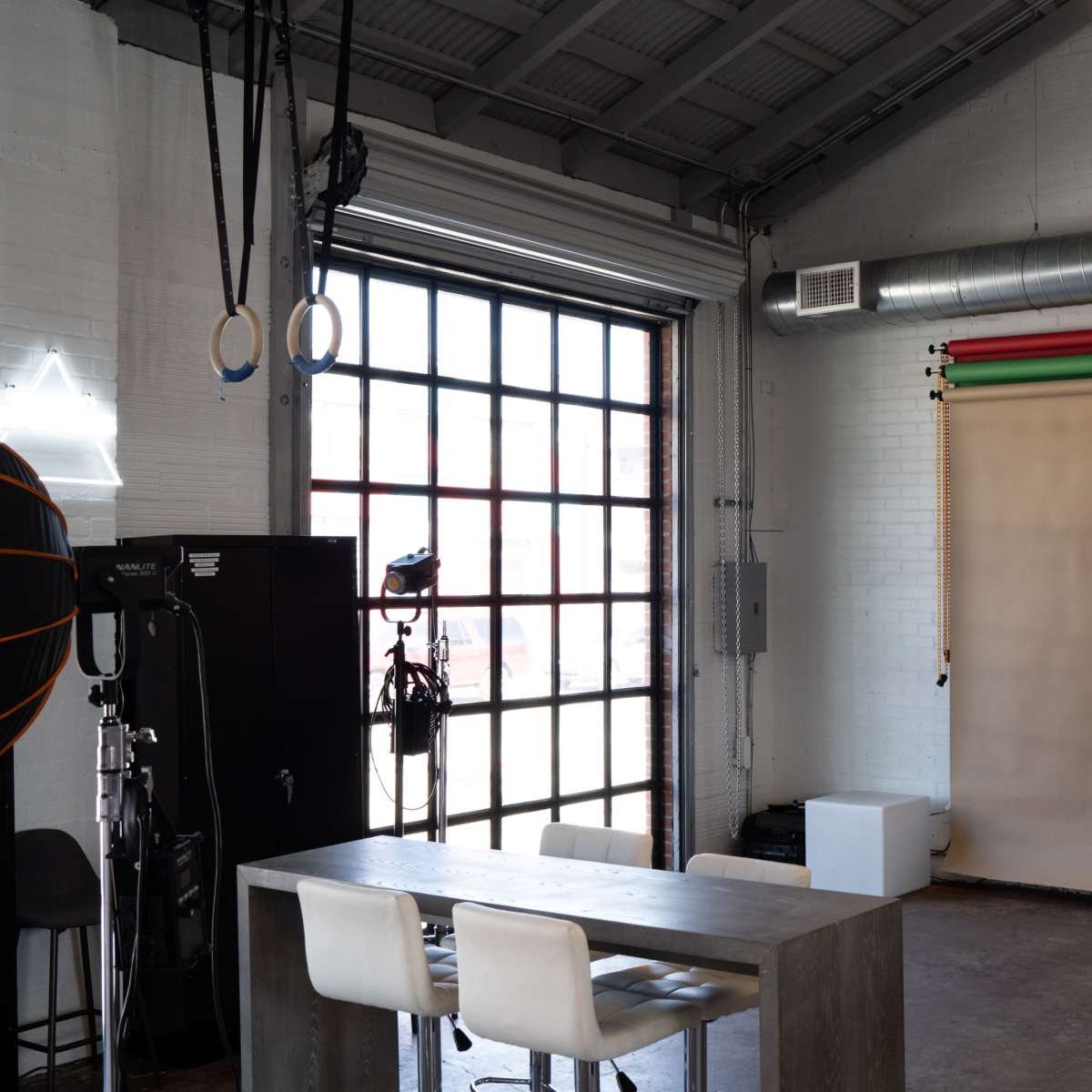 A photography studio featuring a table with chairs, a backdrop setup, and large windows.