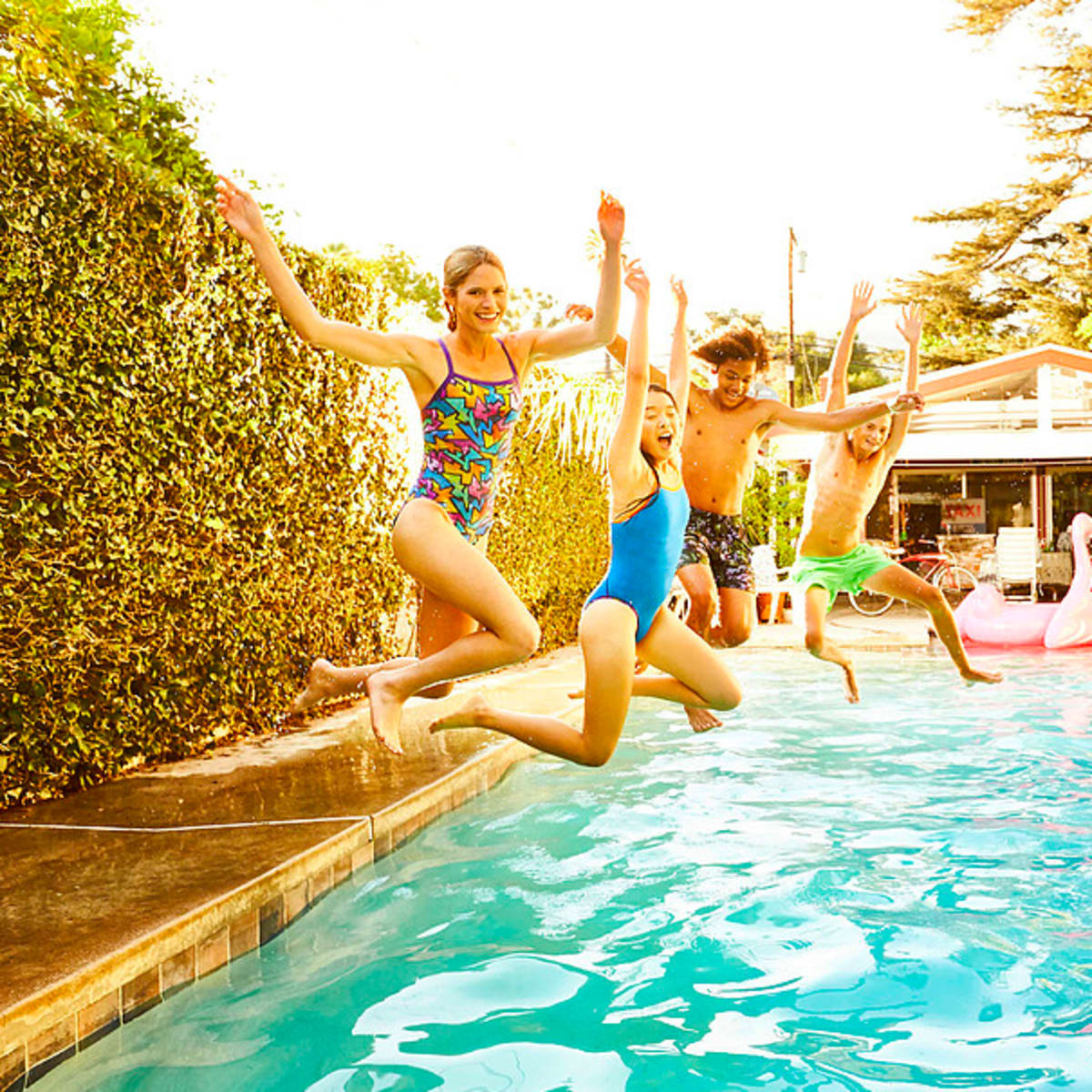 Four children jump into a swimming pool on a sunny day.