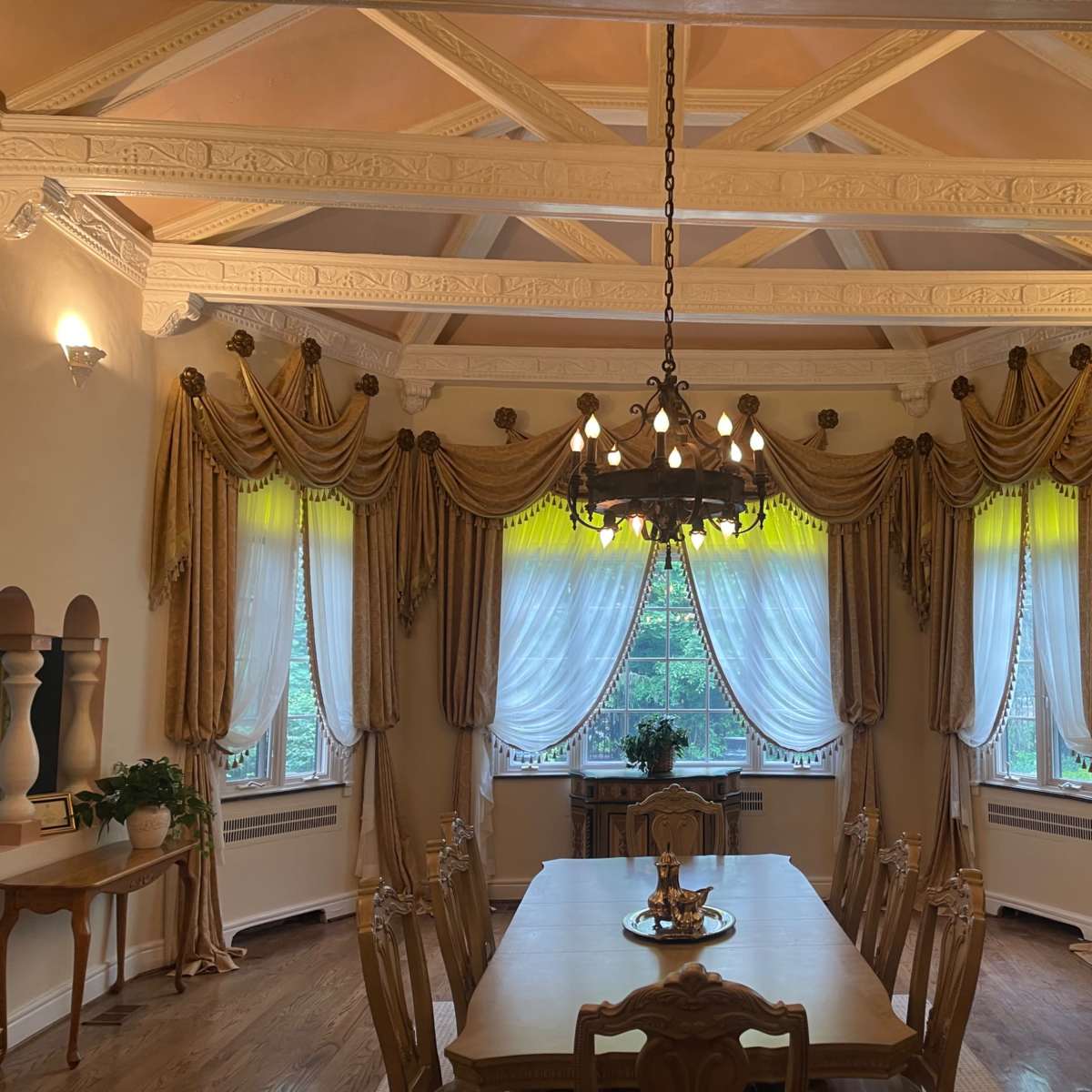 A dining room with a large table, ornate ceiling, decorative curtains, and a chandelier.