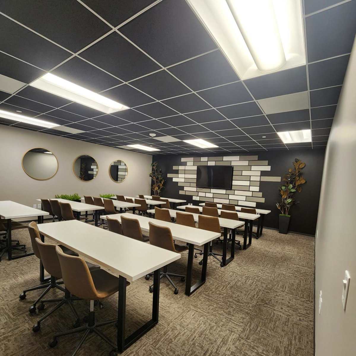 A modern classroom setup with multiple rows of white tables and brown chairs, featuring a wall mounted screen and decorative elements.