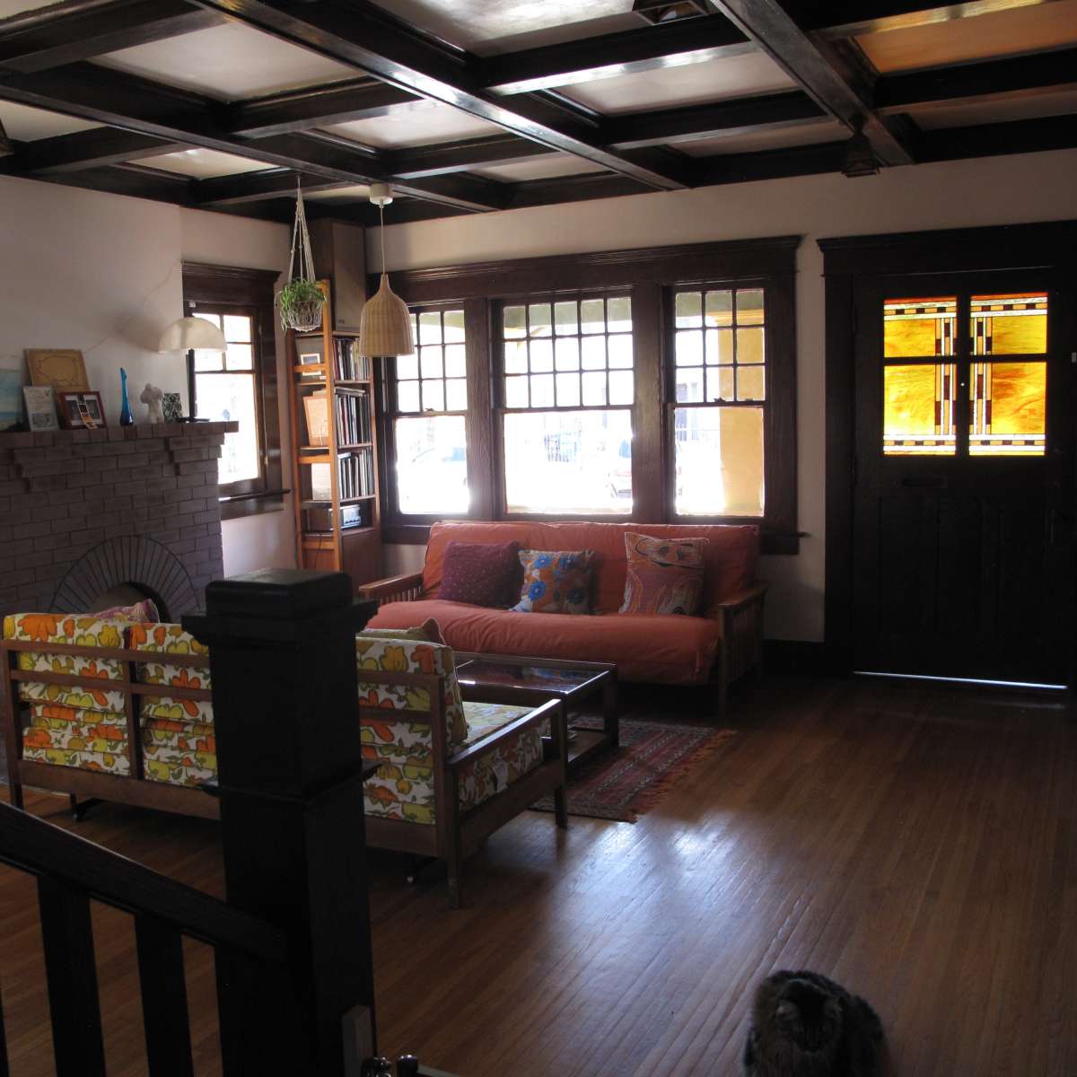 A living room featuring a brick fireplace, a patterned sofa, and a door with stained glass windows.