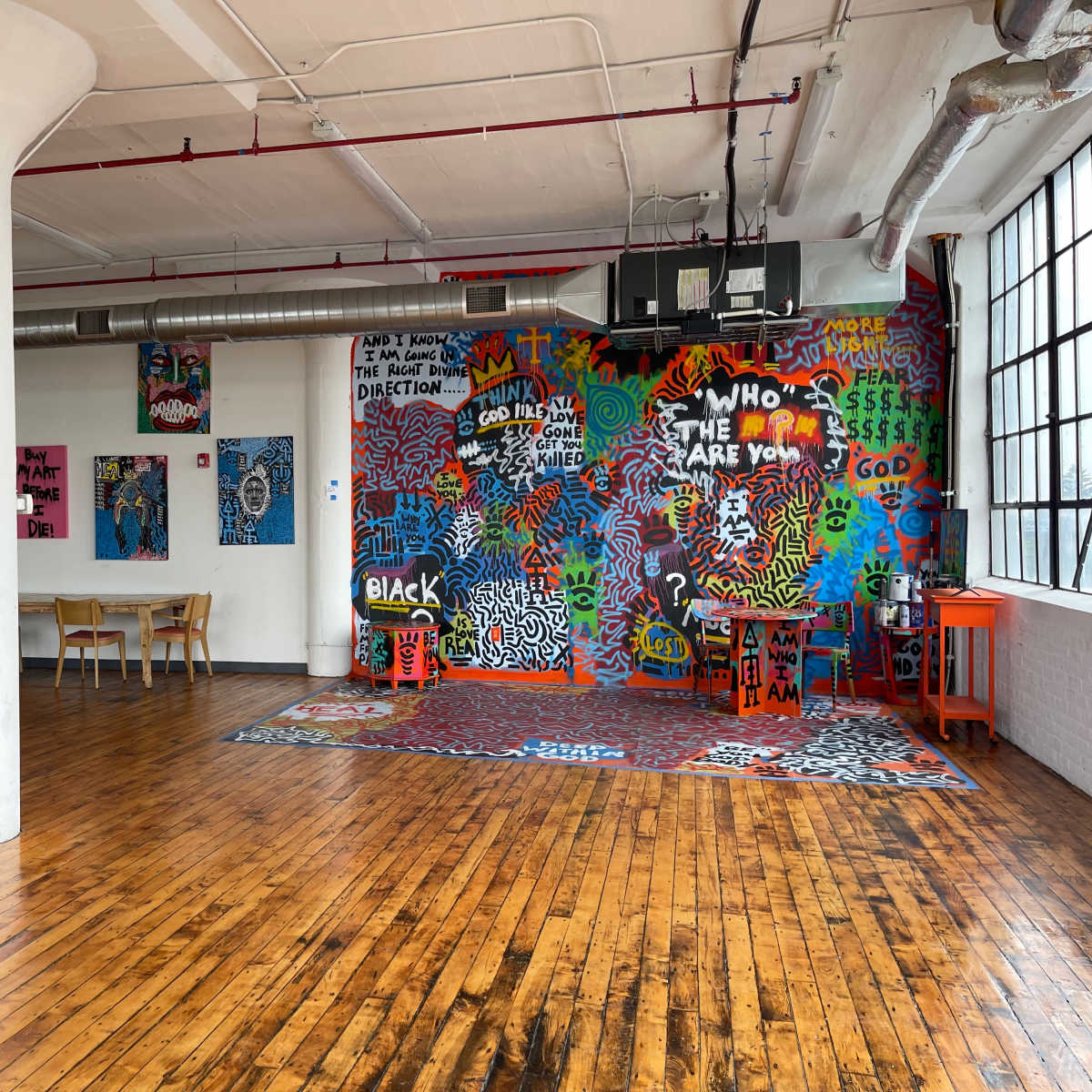 An industrial-style room with wooden floors, featuring a colorful graffiti-covered wall and several tables and chairs arranged in the space.
