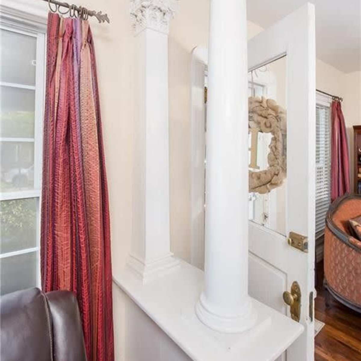 A corner of an interior space featuring two white columns, a doorway, and red curtains on a window.