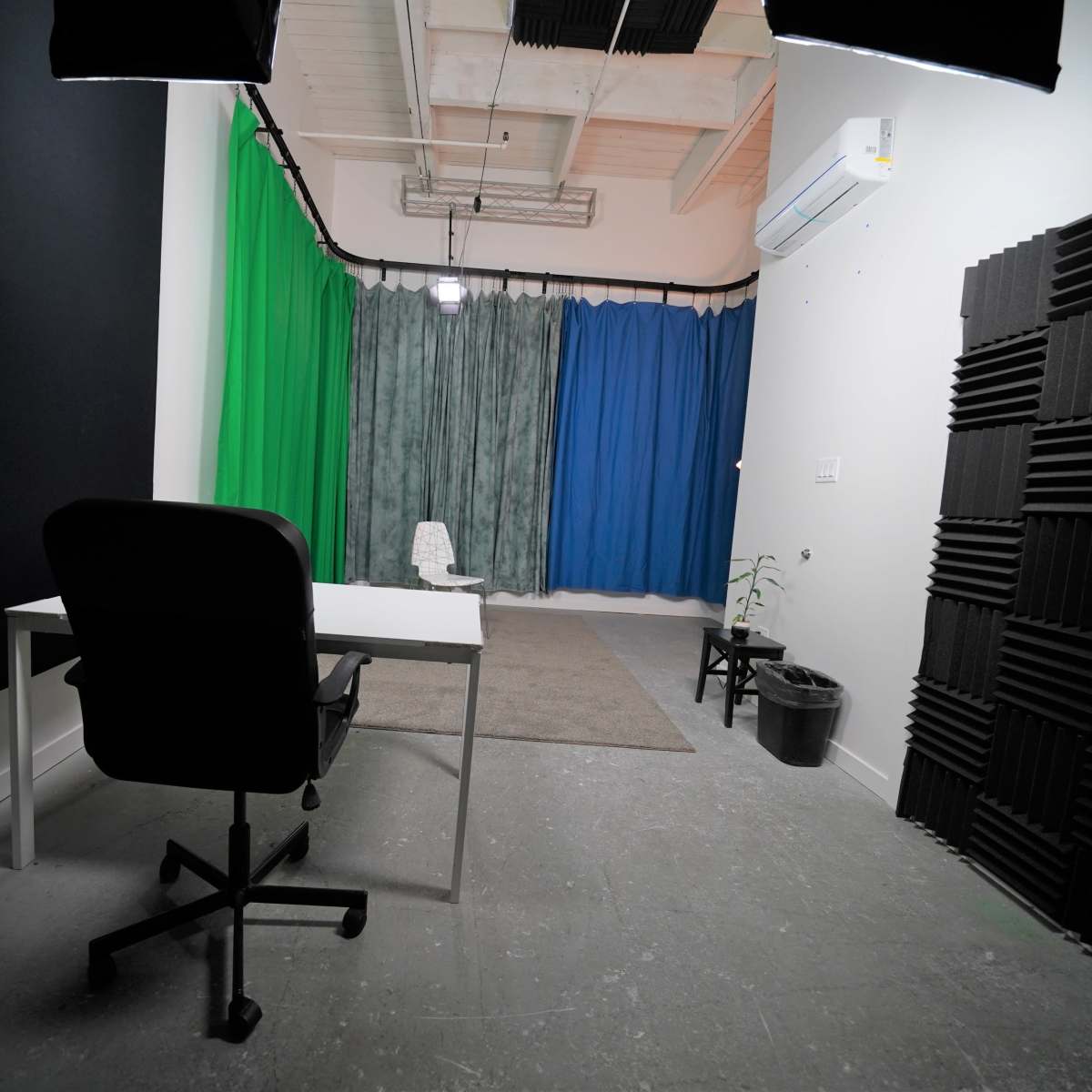A studio space with a desk and chair in front, surrounded by colored curtains and soundproofing panels.