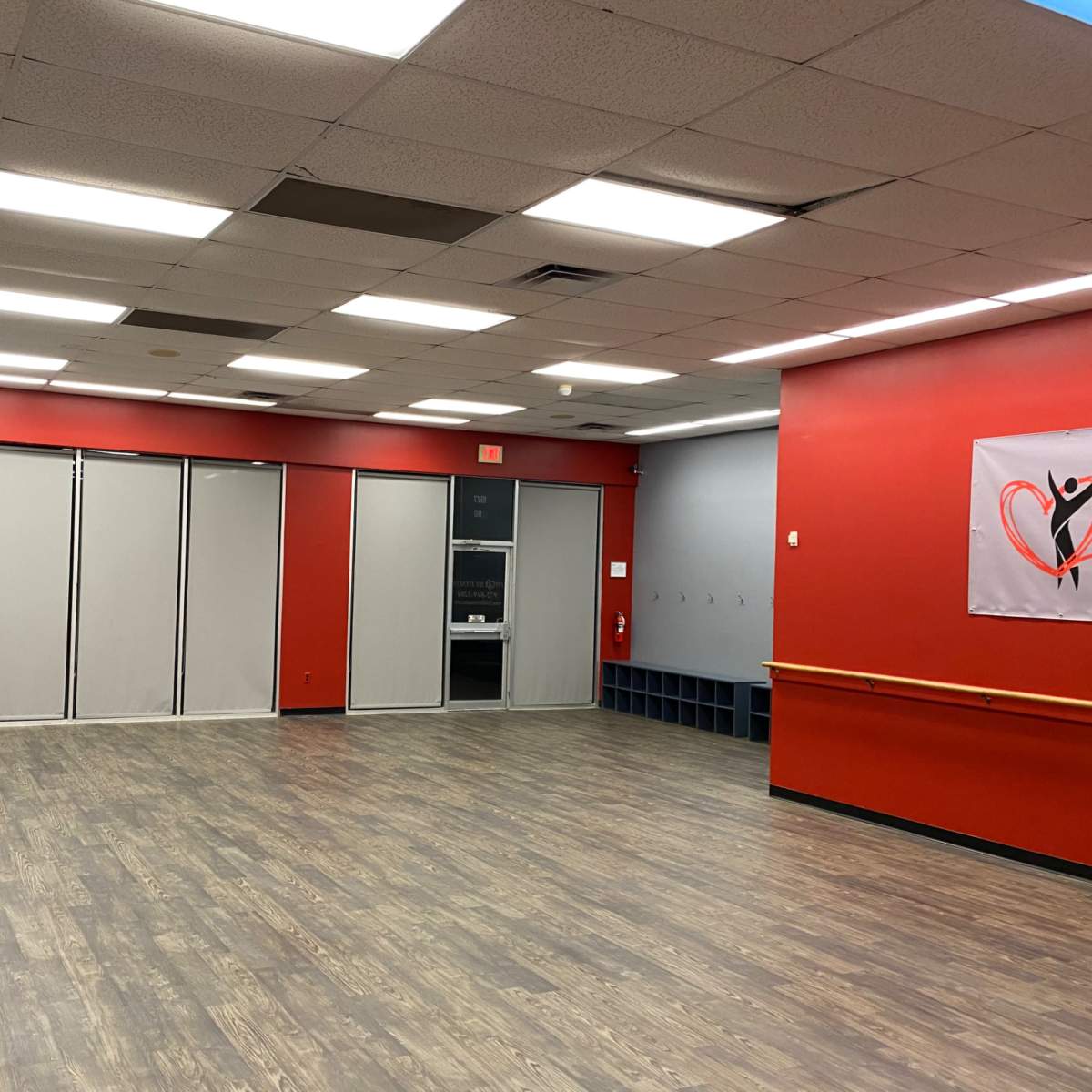 An empty dance studio with a mirrored wall, red painted walls, and a wooden floor.