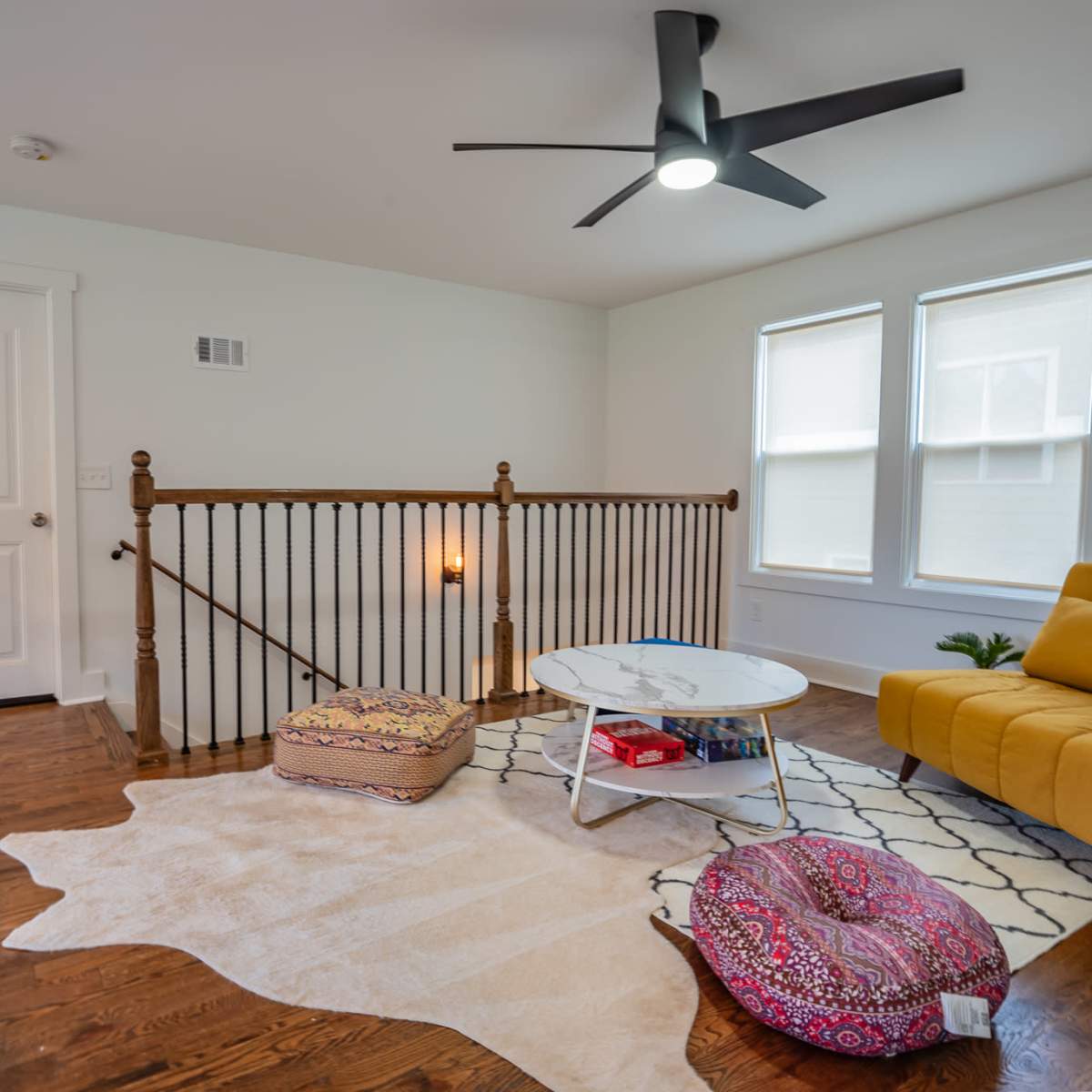 A modern upstairs living area with a yellow couch, a round coffee table, and a patterned rug on wooden flooring.