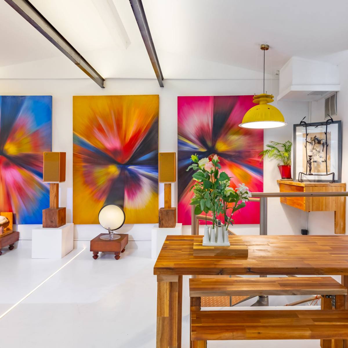 A well-lit art studio features a wooden table surrounded by colorful abstract paintings, a globe, and modern decor.