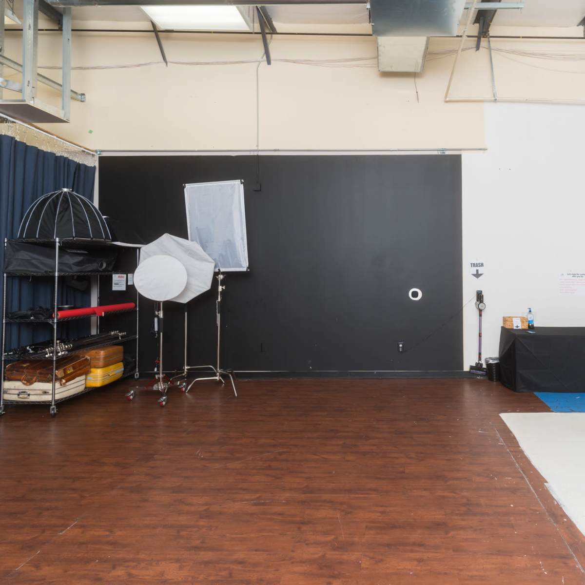 A spacious photography studio with a wooden floor and various equipment, including a backdrop, lighting setups, and a table.