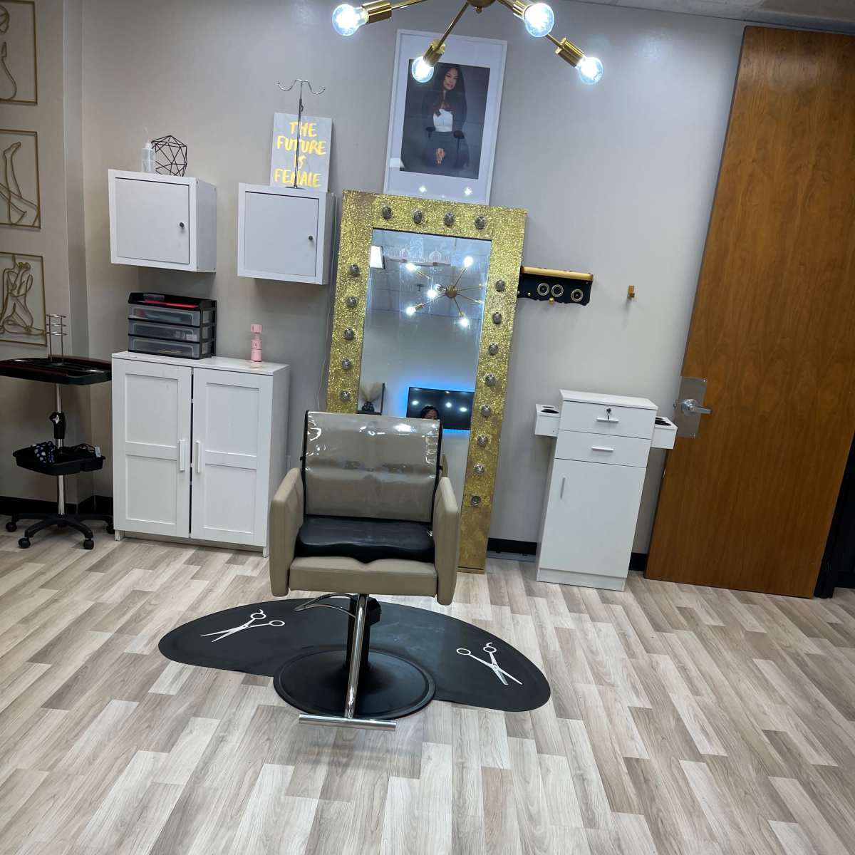 A salon or spa interior featuring a stylish chair, a large mirror with decorative lighting, and various cabinets and equipment on the walls.