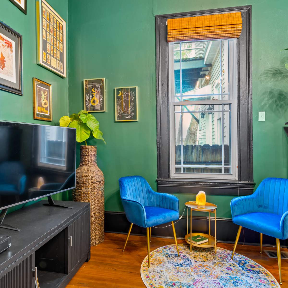 A cozy room with green walls, a television, a record player, two blue chairs, a small golden table, and framed artwork.
