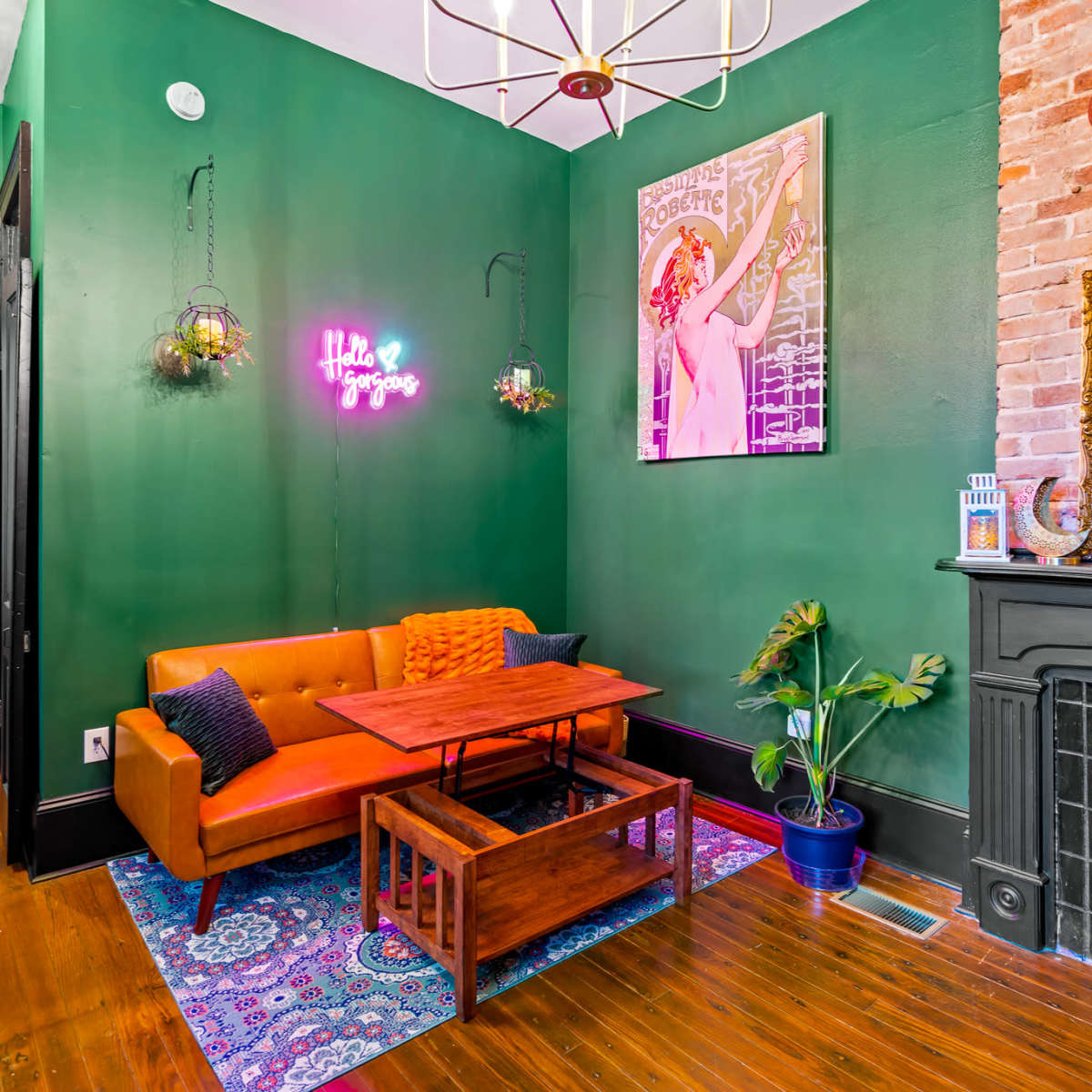 A room with green walls, featuring an orange couch, a wooden coffee table, and decorative plants near a fireplace.