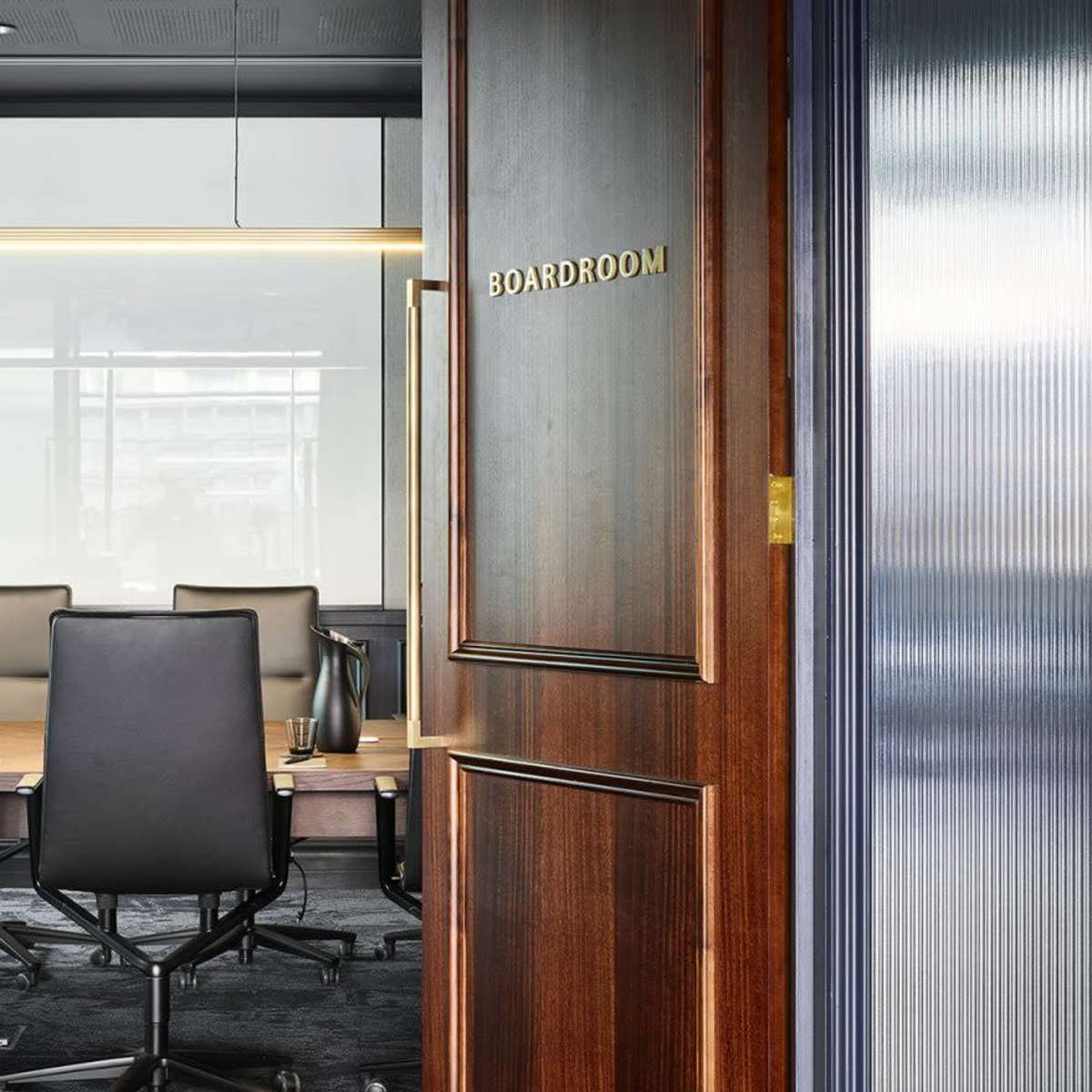 A modern boardroom with a long table and ergonomic chairs, viewed through open wooden double doors.