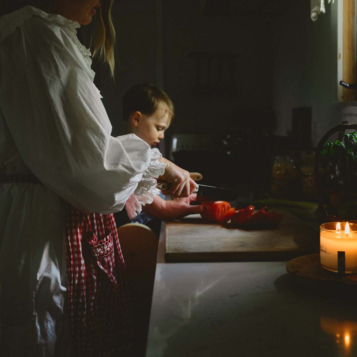 A woman in a white blouse slices tomatoes on a kitchen counter while a boy watches.