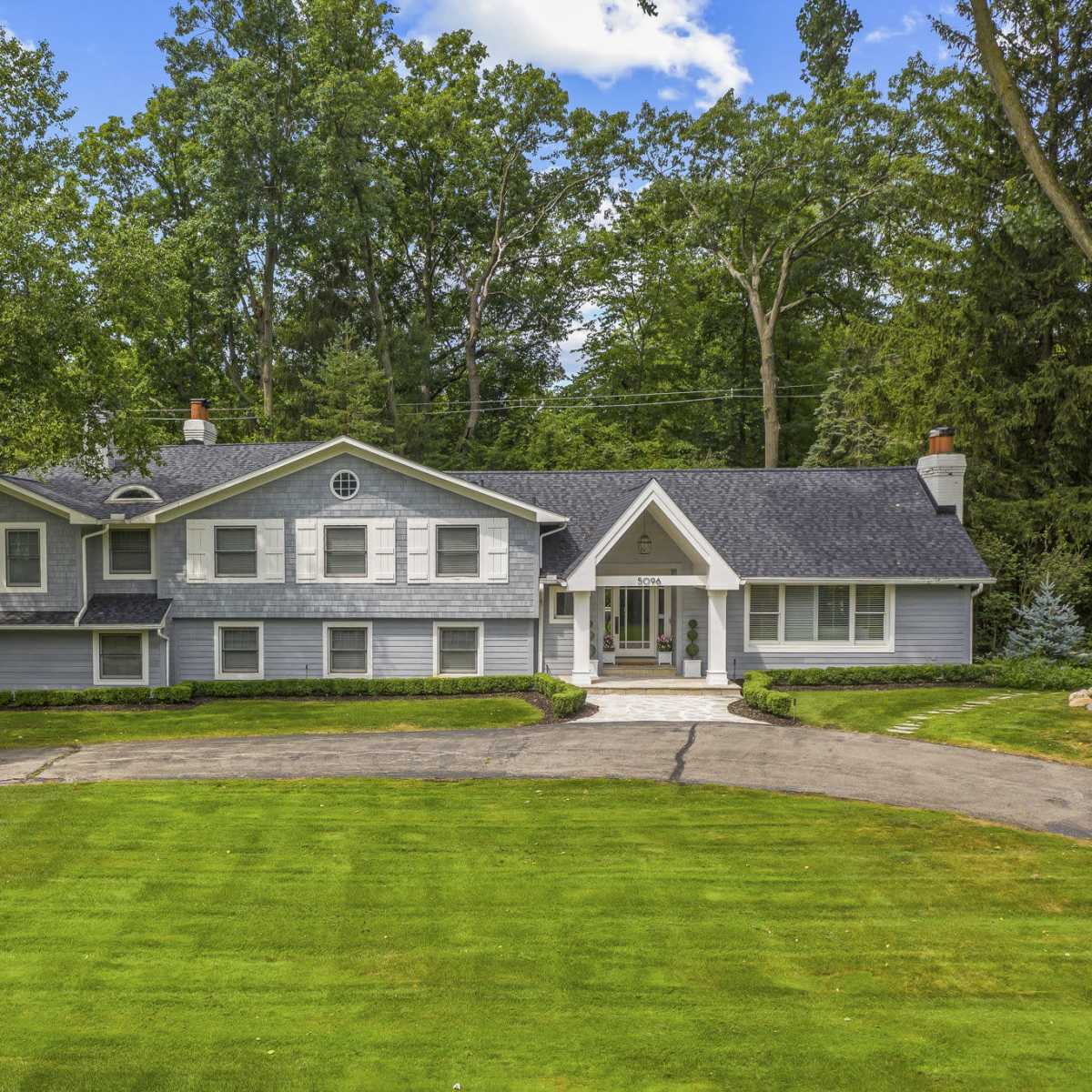 A large, two-story gray house with multiple windows situated on a manicured lawn surrounded by trees.