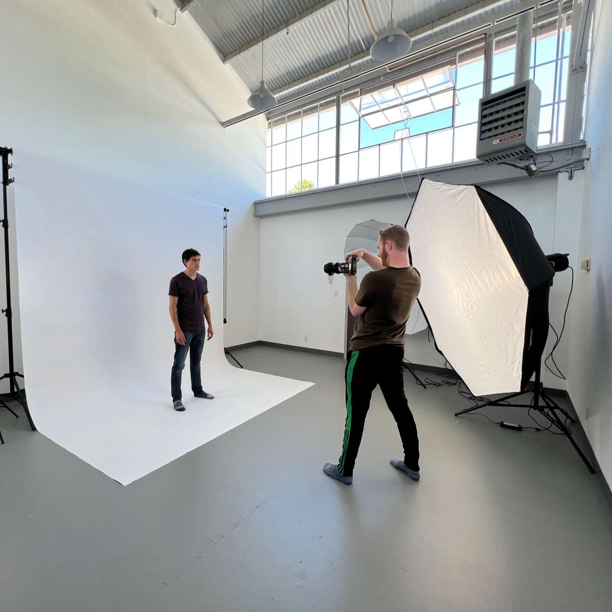 A photographer is capturing images of a model in a studio with a white backdrop and various lighting equipment.
