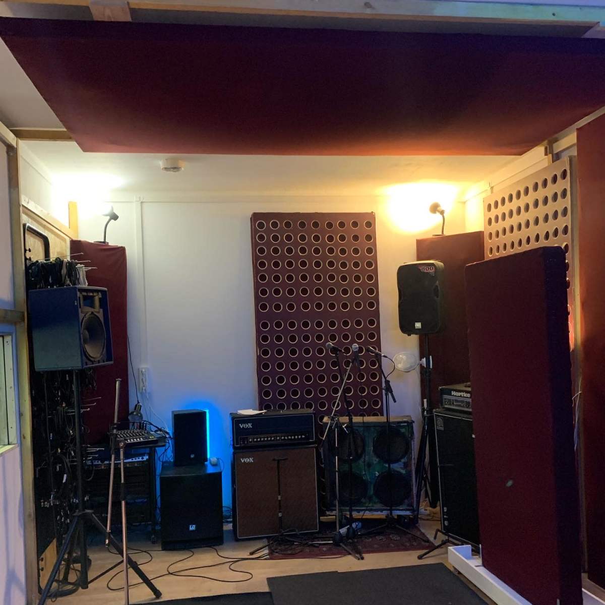A music rehearsal studio with microphones, amplifiers, and soundproofing panels arranged in the space.