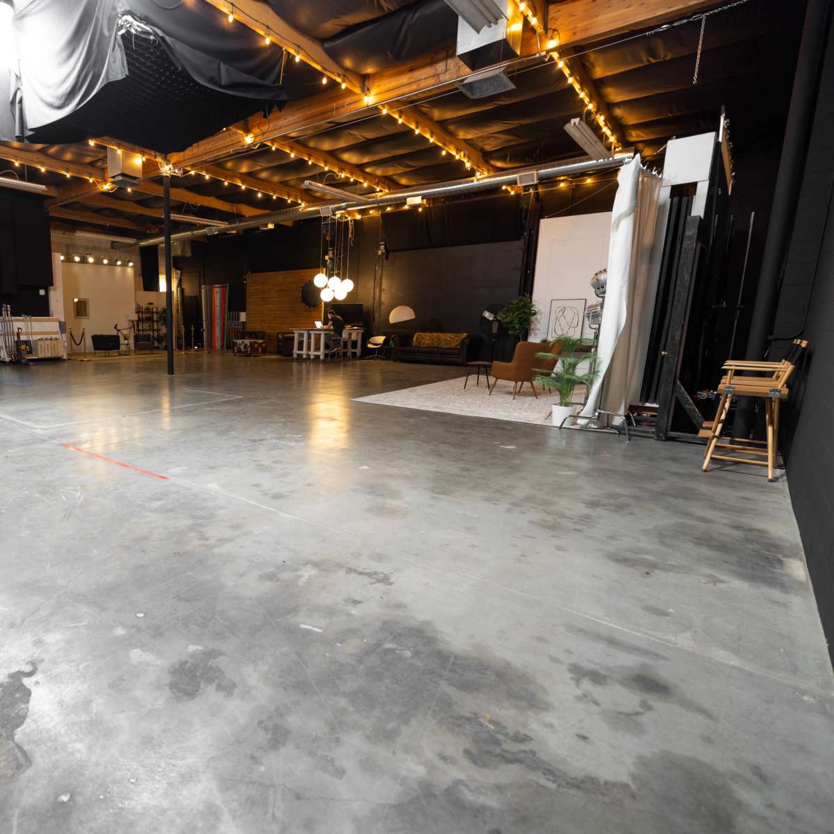 A spacious film studio with concrete flooring, black walls, and various equipment arranged along the edges.