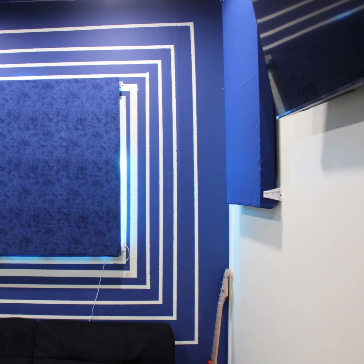 A blue wall with concentric white stripes and a blue curtain in the center, above a black sofa.