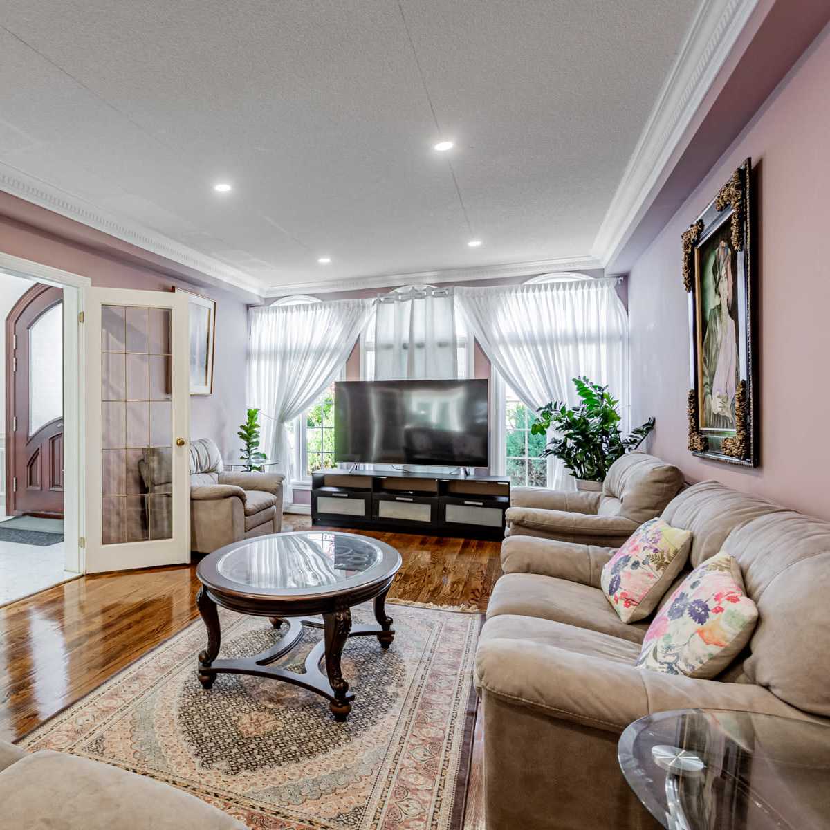 A living room with beige sofas, a round coffee table, and large windows dressed with sheer curtains.