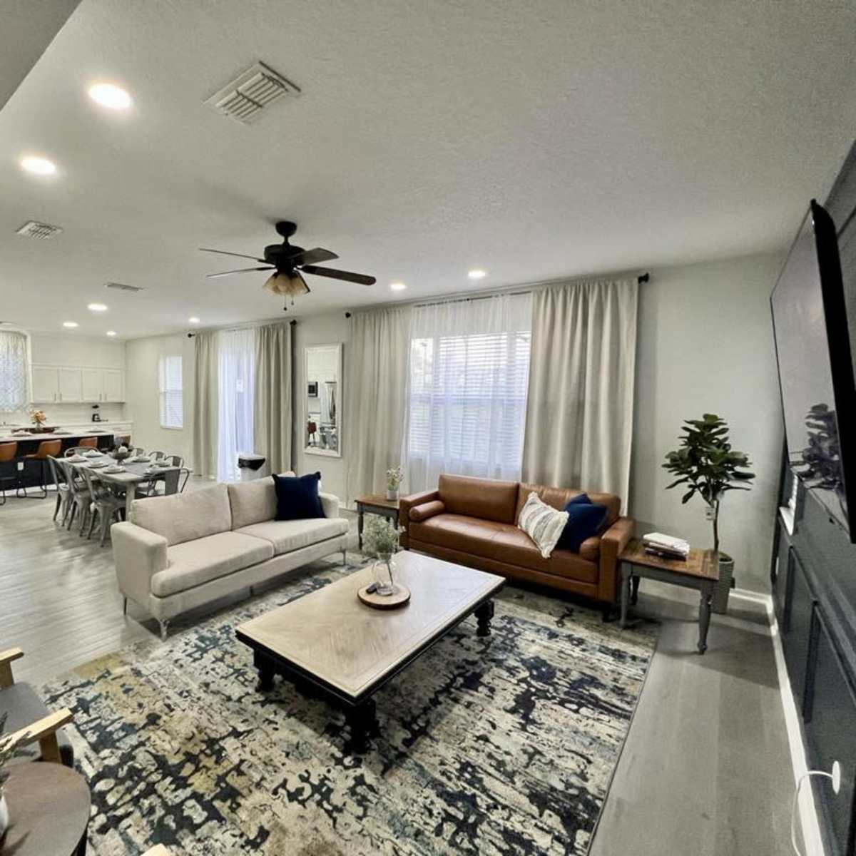 A modern living room with a light-colored couch, a brown leather sofa, a coffee table, and a view of an open kitchen area in the background.