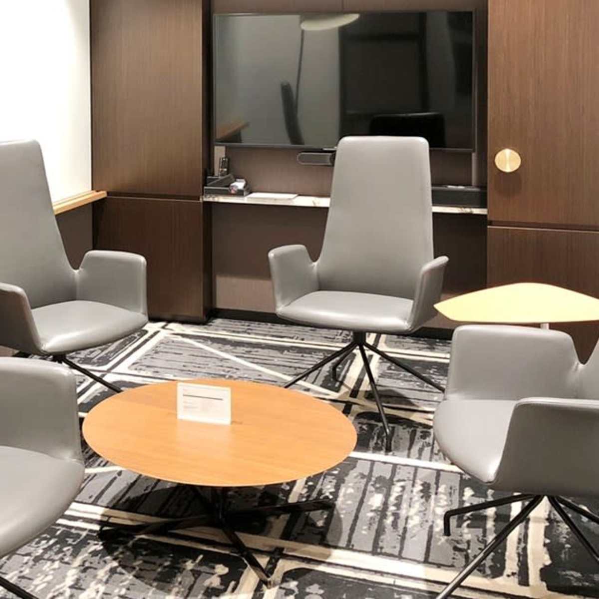 A small meeting room with four gray chairs arranged around a round wooden table on a patterned carpet.