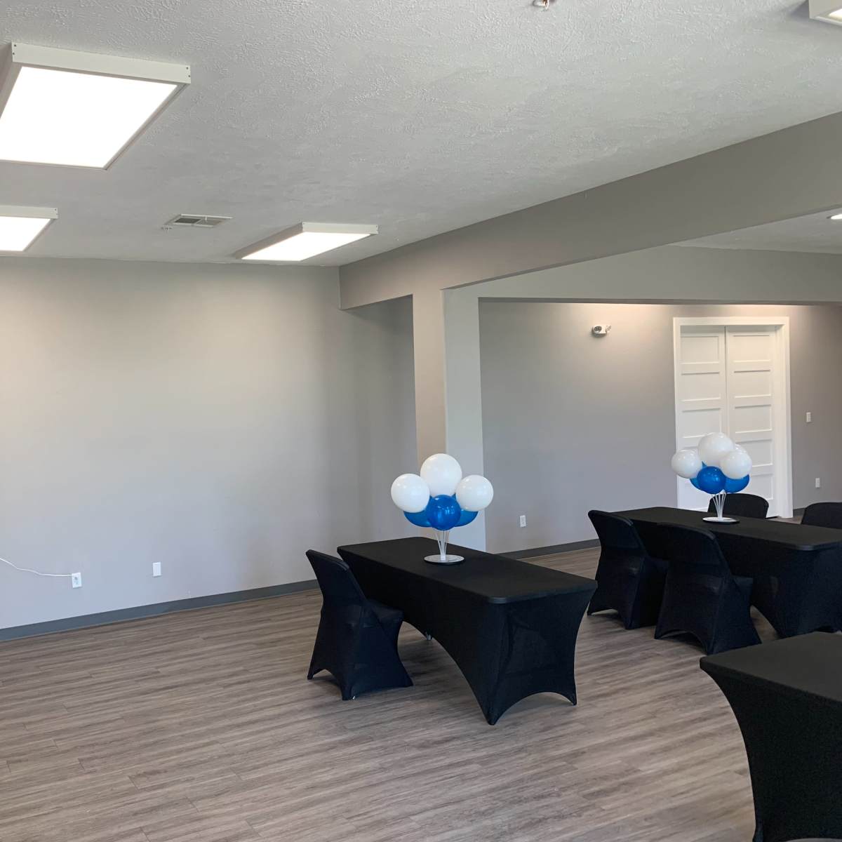 A modern event space with black tablecloths and decorations featuring blue and white balloons.