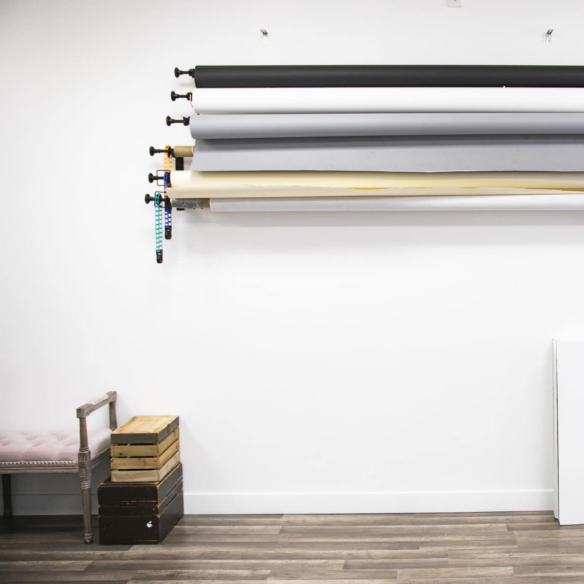 A wall displays several rolls of backdrop material above a wooden crate and a gray chair.