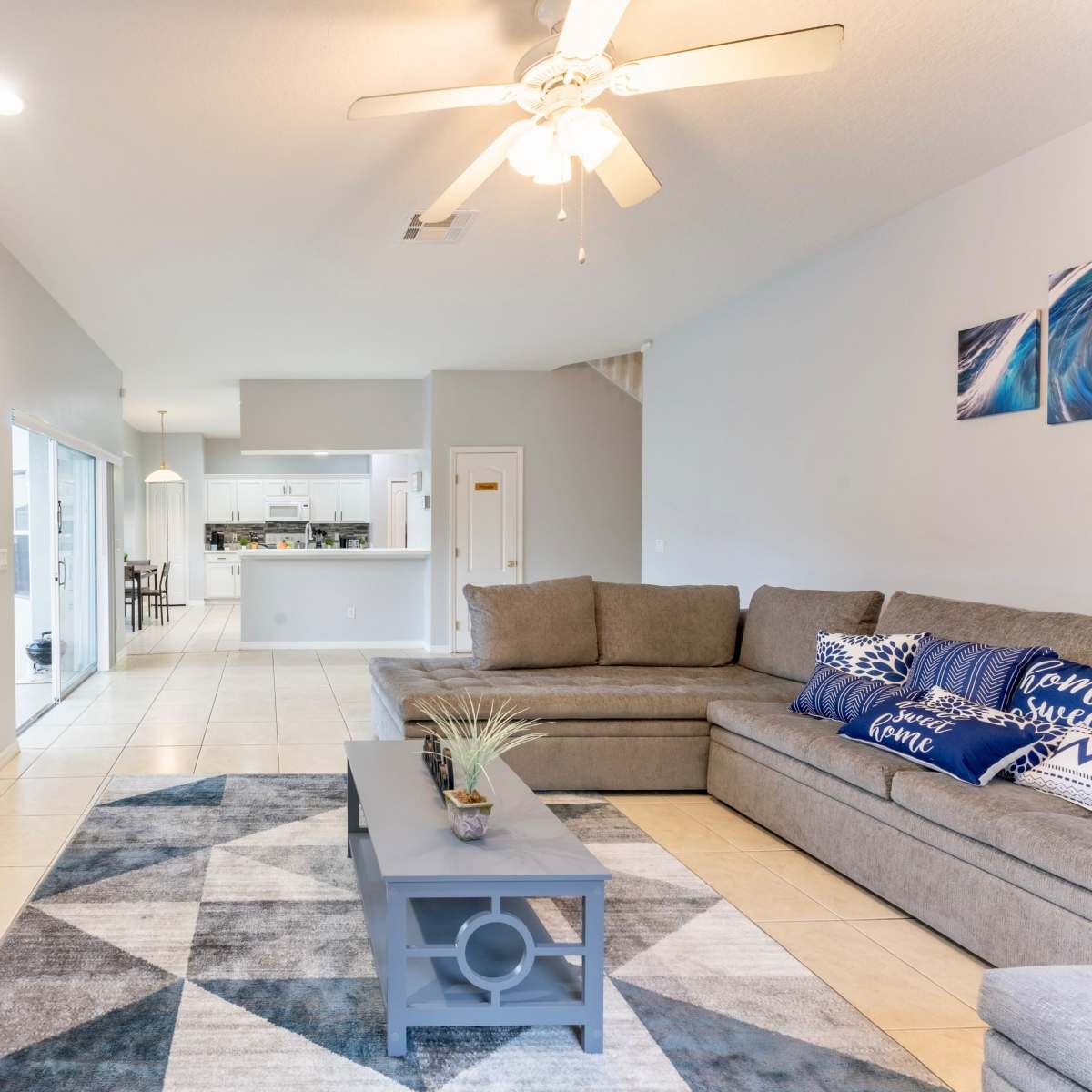 The living room features a large sectional sofa, a coffee table, and a TV mounted on a stone accent wall, with an open view to a dining area behind it.