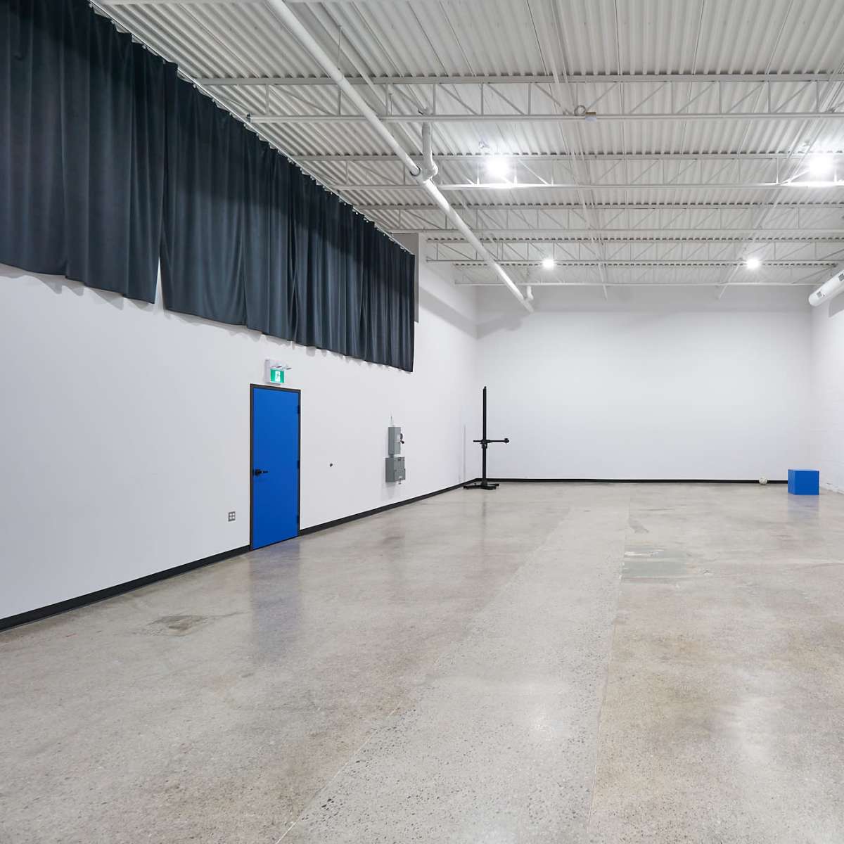 A large, empty gymnasium with polished concrete floors, high ceilings, and a blue door on one wall.