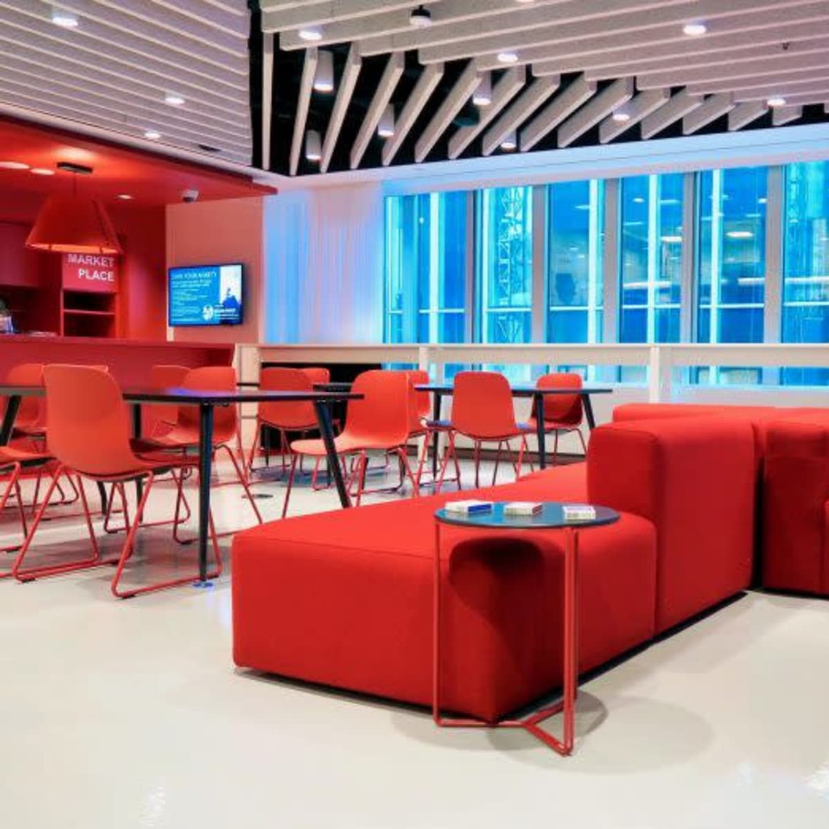 A modern lounge area featuring red furniture, including a sectional couch, a side table, and chairs, in a space with large windows and a bright, open atmosphere.