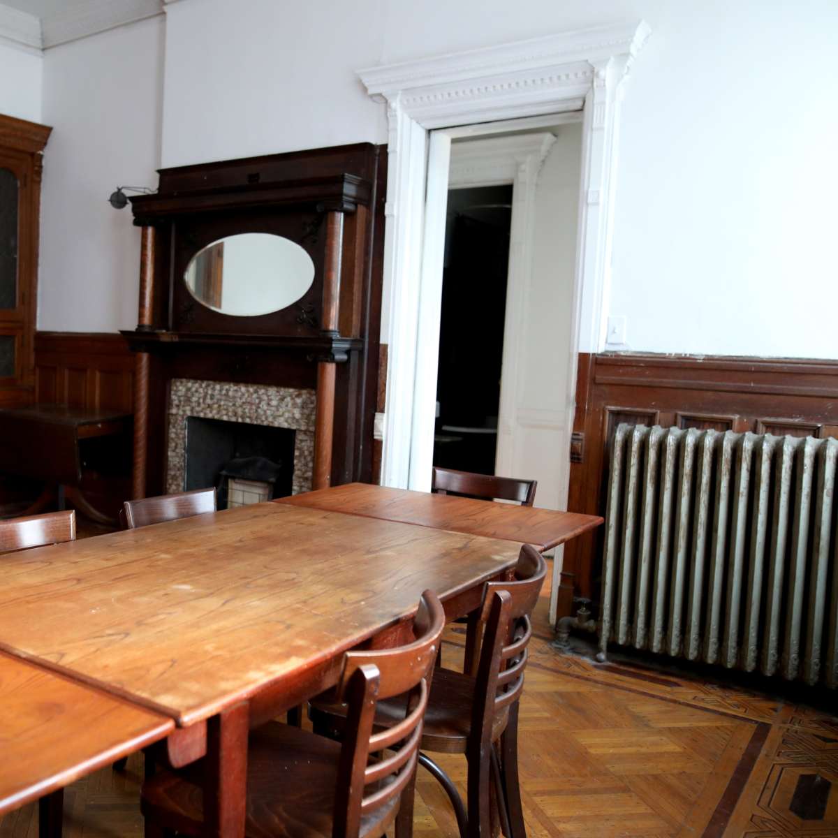 A spacious room with a long wooden table surrounded by chairs, featuring a fireplace and a large mirror on a dark wooden mantel.