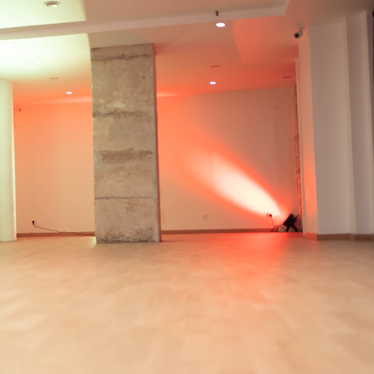 An empty room with stone walls, wooden flooring, and colored lighting coming from the ceiling.
