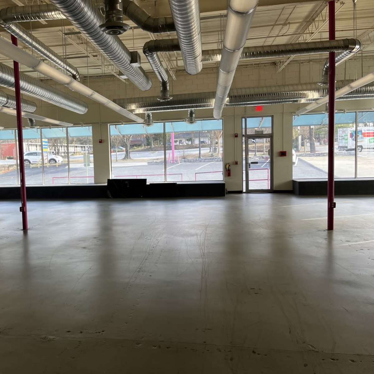 An empty interior space with concrete flooring and large windows allowing natural light to enter.