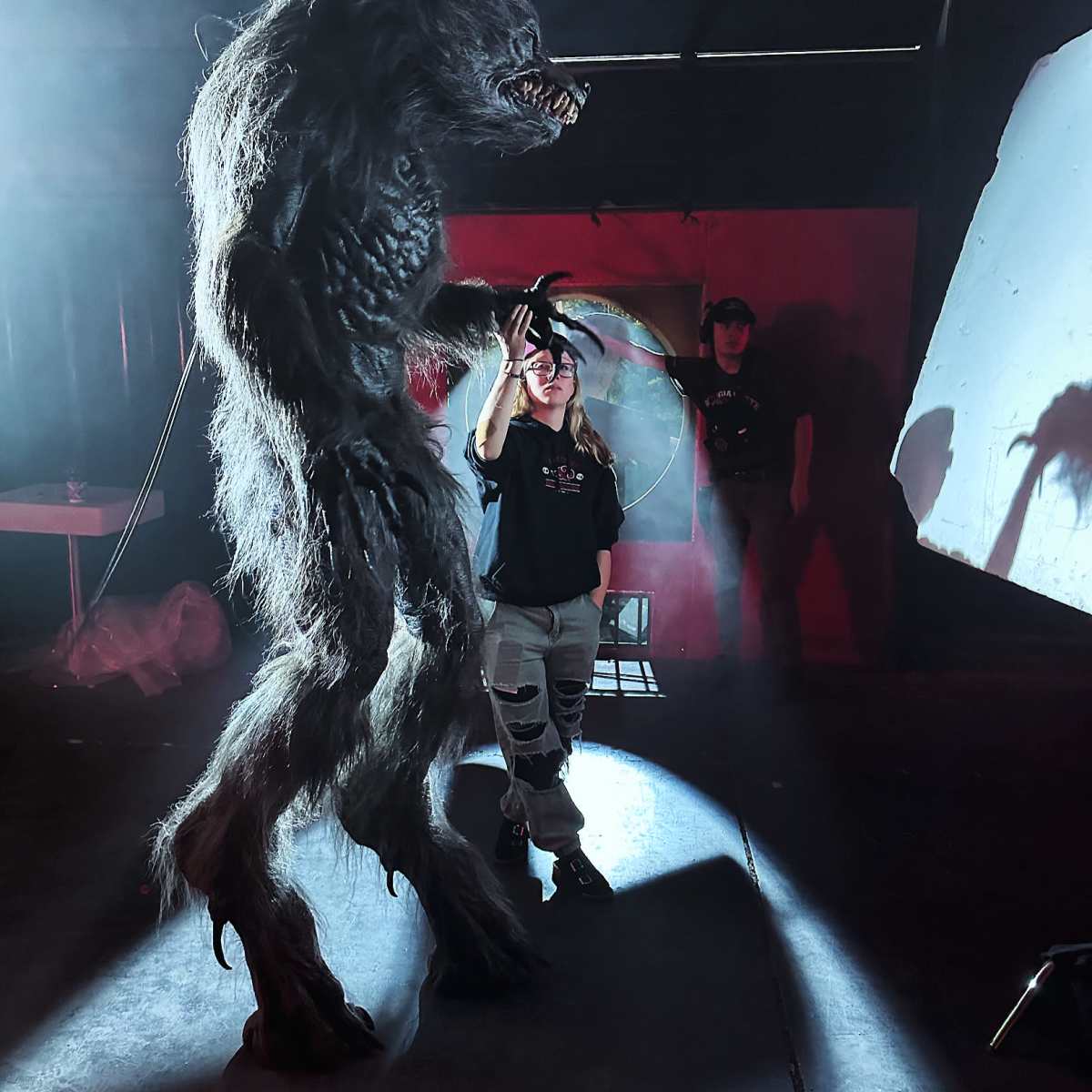 A person stands next to a large, beast-like figure in a dimly lit space with mist.
