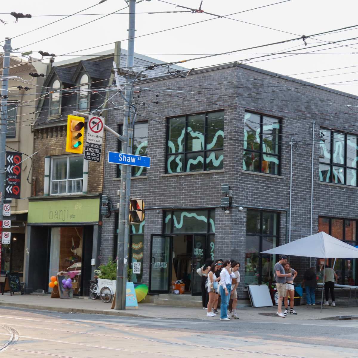 A street corner with a modern building featuring large windows and multiple vendors under blue tents selling goods.