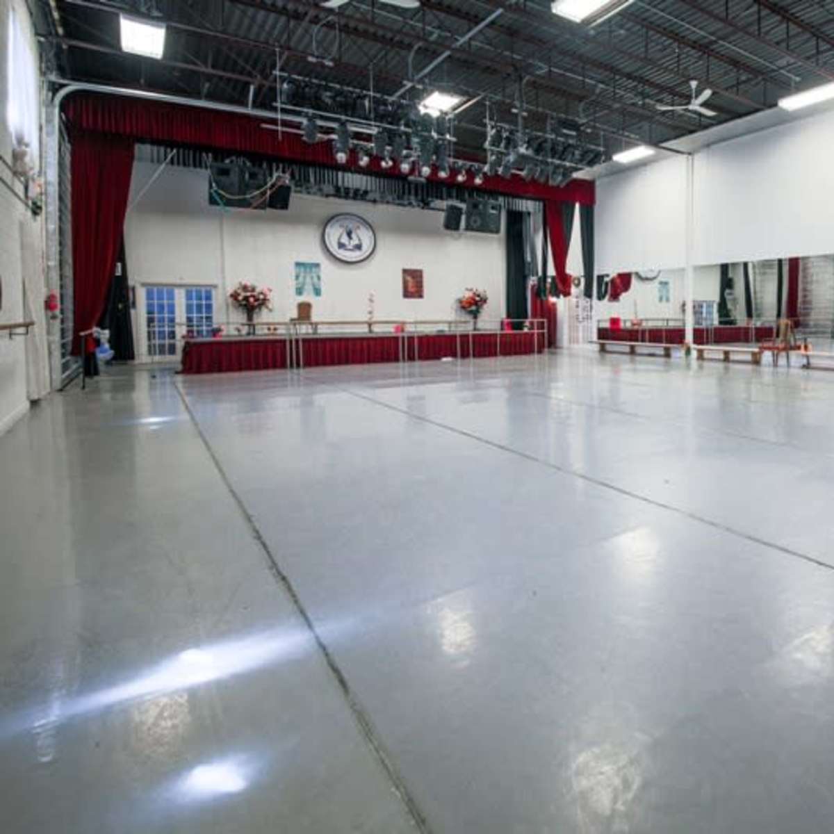 A spacious dance studio with a wooden barre, mirrored walls, and a stage area at one end.