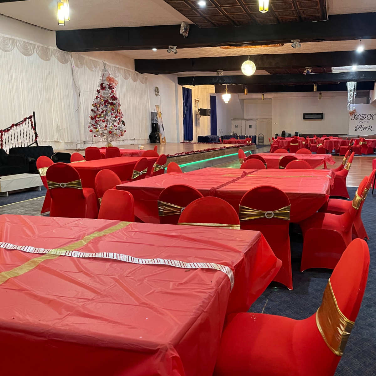 A banquet hall set up with numerous red tables and chairs, decorated for an event.